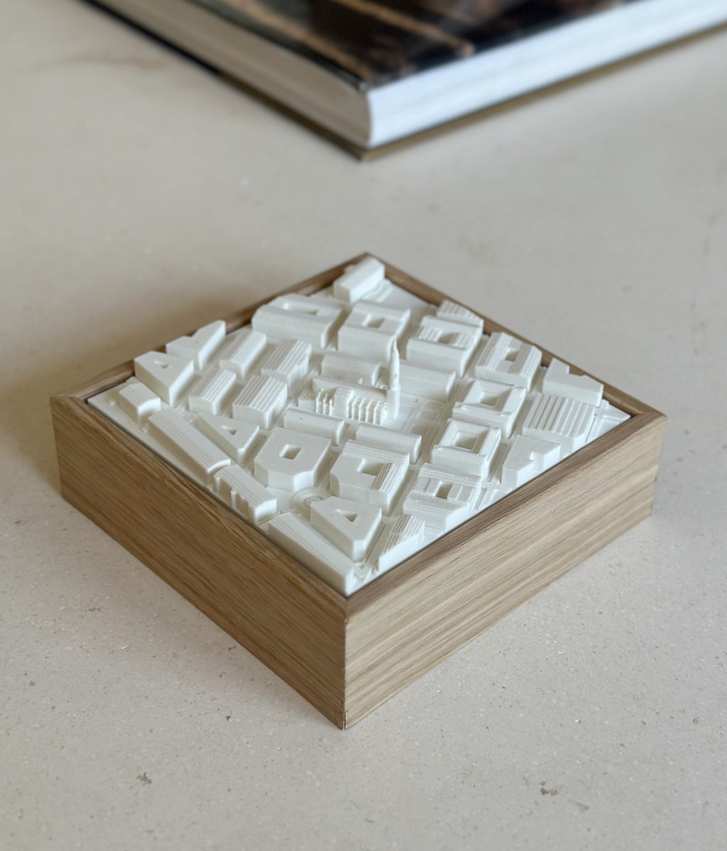 3D city map artwork in a wooden frame, minimalist urban decor on a beige table.