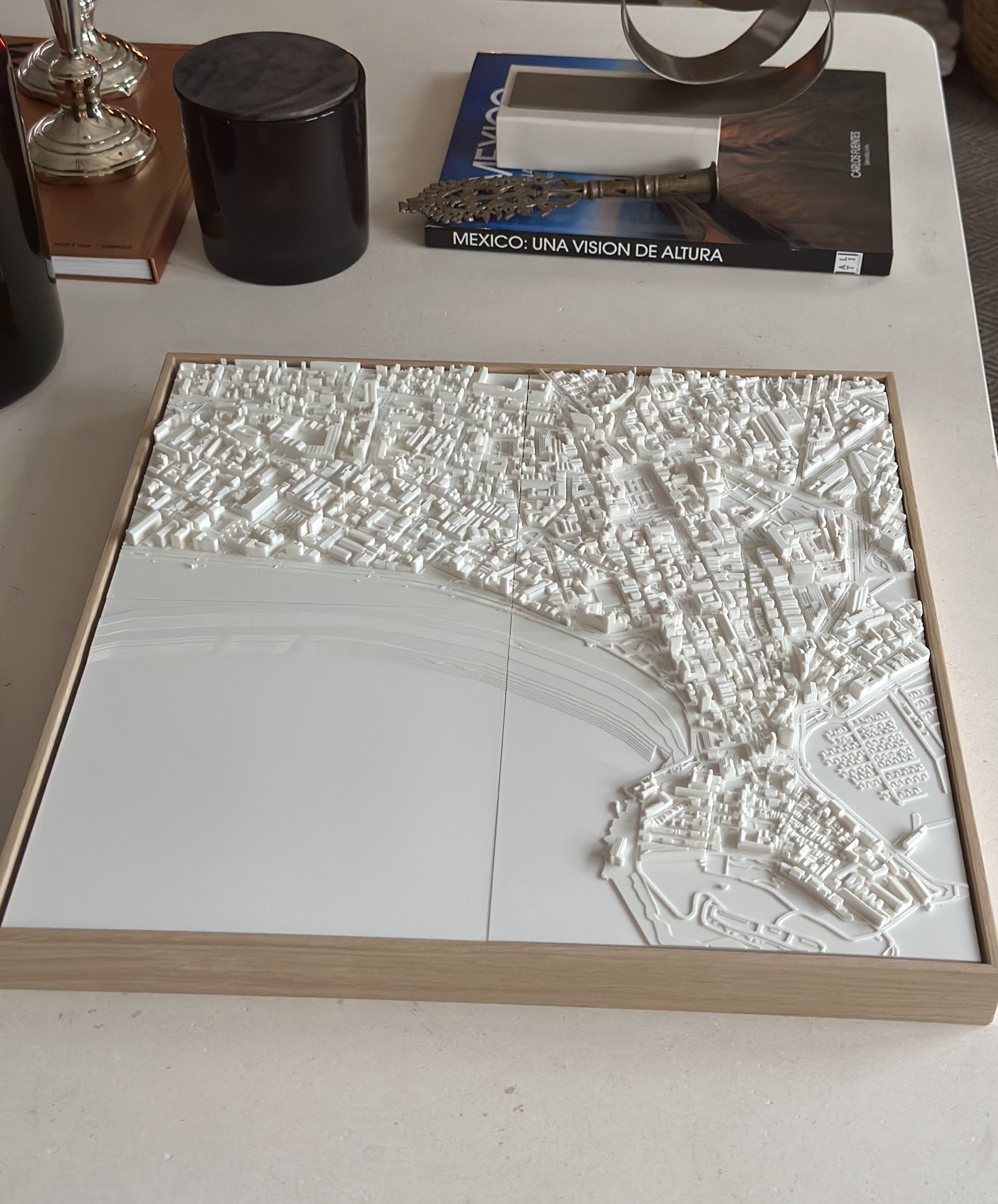 3D city map wall art with intricate white buildings on a wooden frame, displayed on a table.