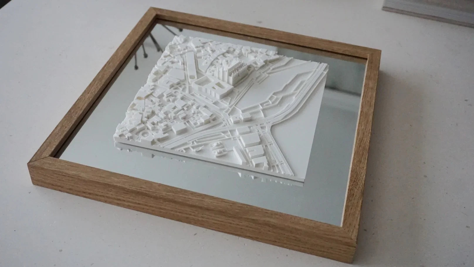Framed 3D city map wall art with white buildings, mirrored background, and wooden frame