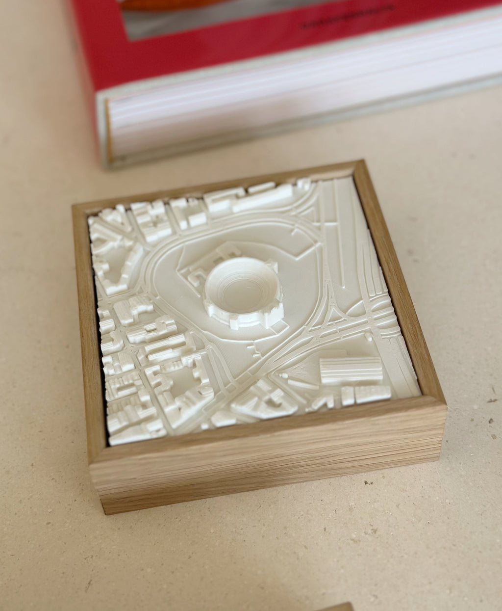 Framed 3D city map model in white, featuring buildings and streets, on a beige surface