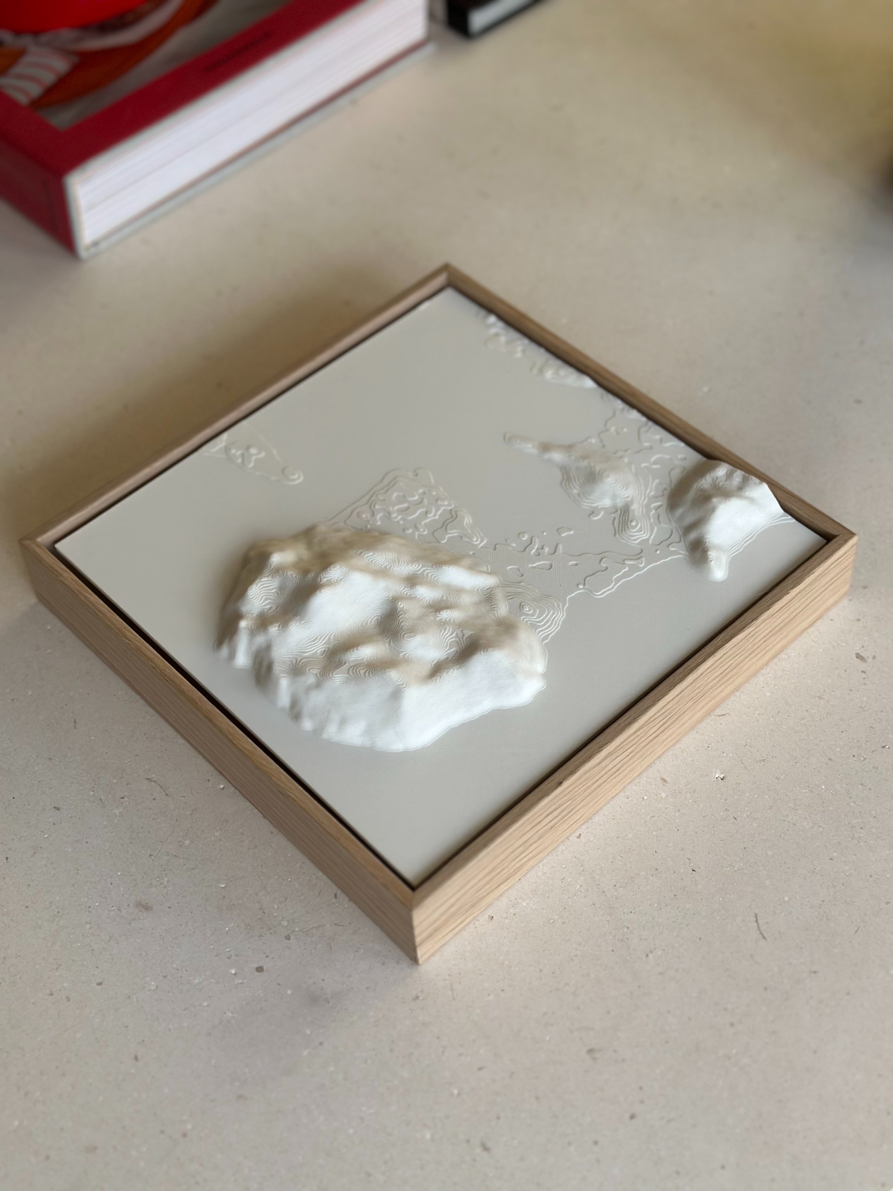 3D city map wall art in a wooden frame on a light surface, topographic decor piece