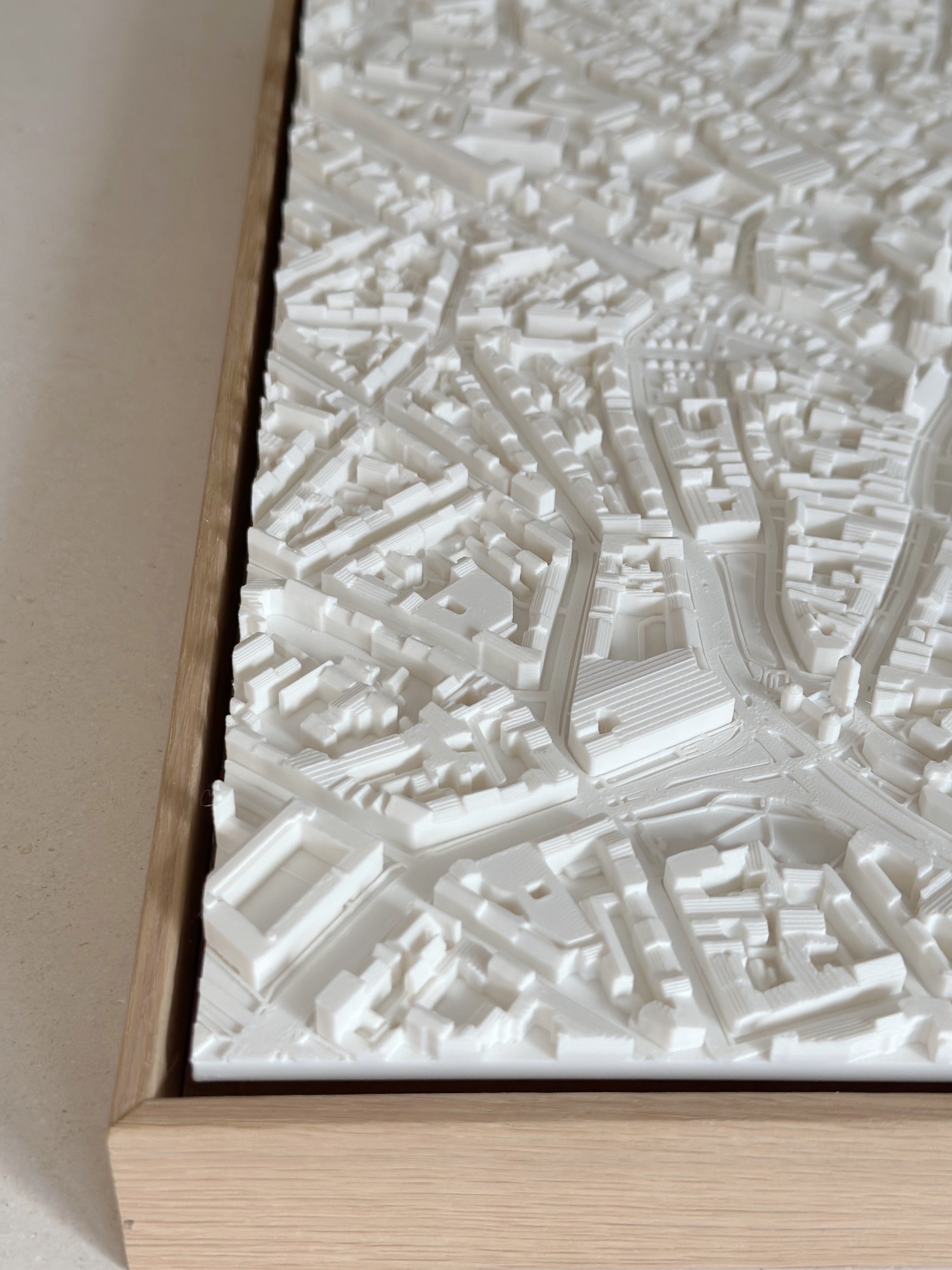 Detailed 3D city map art in white relief, framed with light wood, ideal wall decor