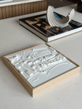 3D city map wall art in a wooden frame on a modern table next to a book and decorative object