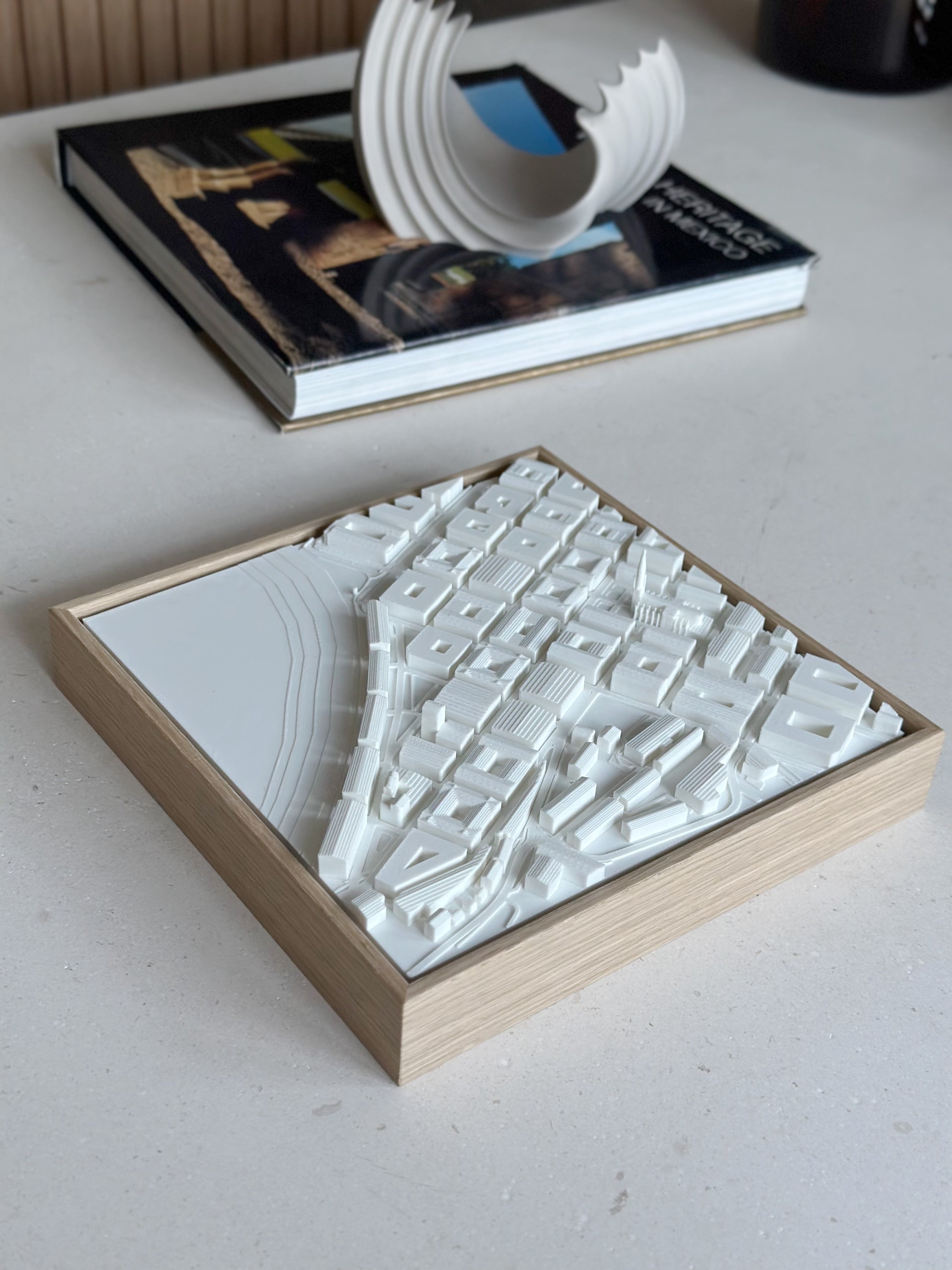 3D city map wall art in a wooden frame on a modern tabletop, decorative book and sculpture nearby