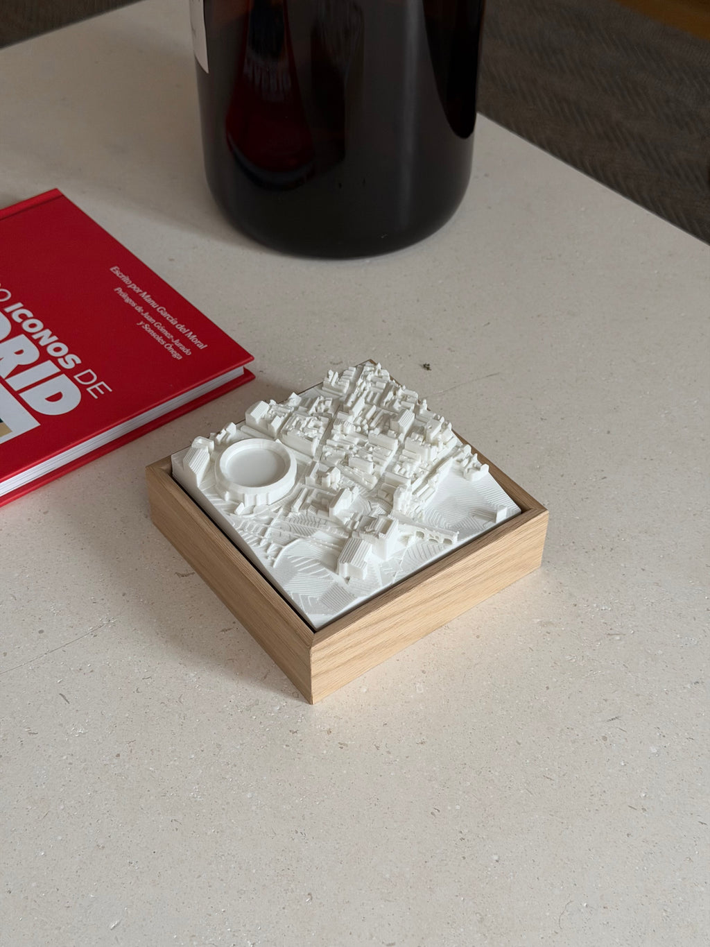 3D city map of Madrid in a wooden frame on a table beside a red book