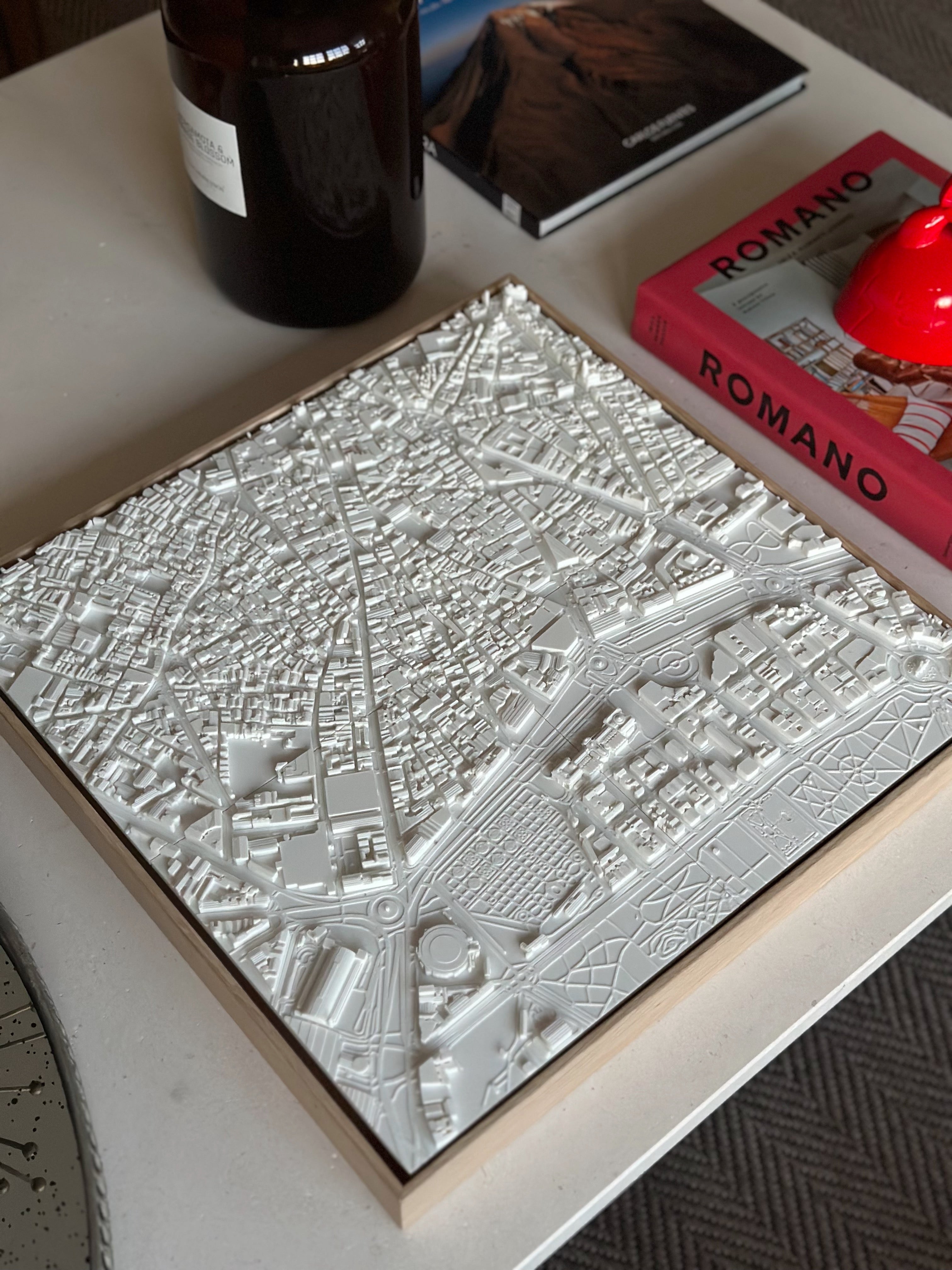 3D city map wall art in white on a table, surrounded by books and decor items