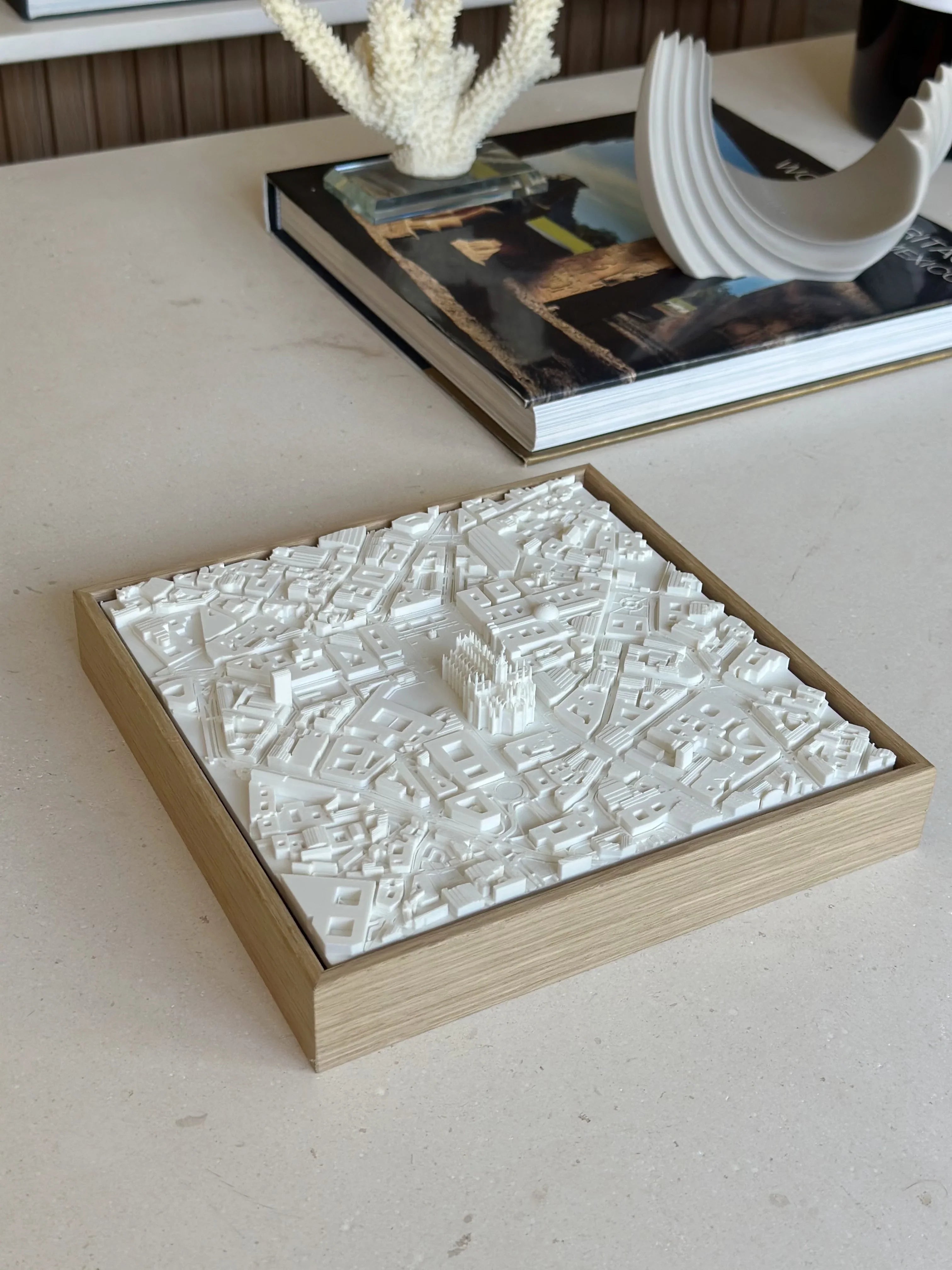 3D city map decor in a wooden frame on a modern table, with books and sculpture nearby