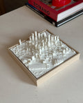 3D city map wall art in white frame on beige table, with books in the background