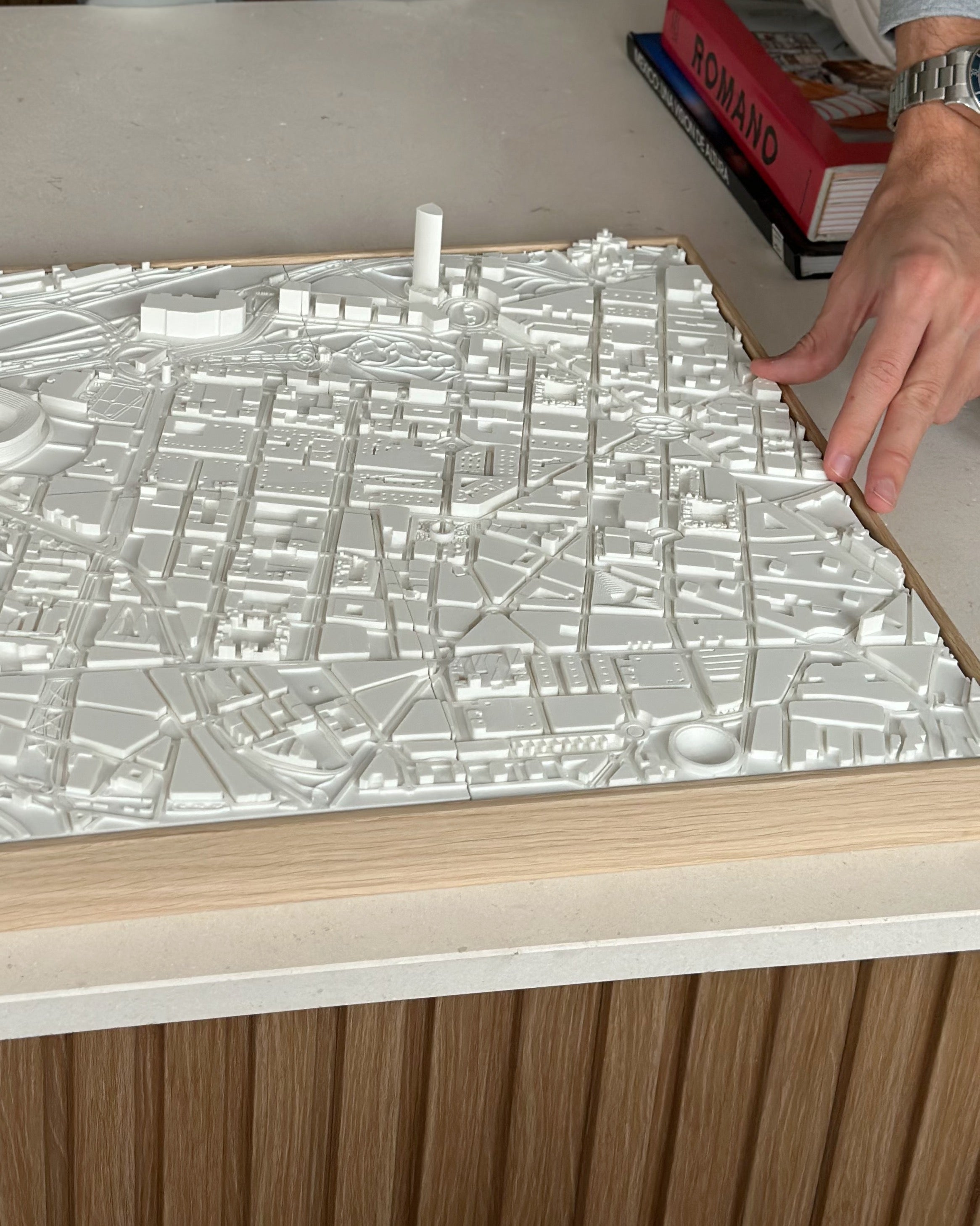 Person assembling a white 3D city map artwork with wooden frame on a table