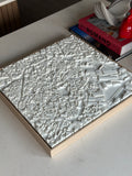 3D city map wall art in white on a wooden frame, modern decor on a table with books