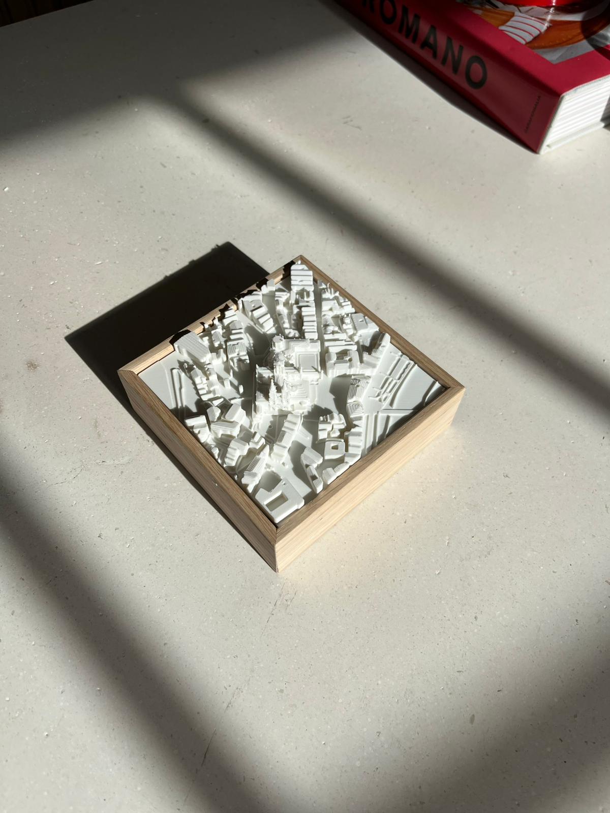 Mini 3D city map art in a wooden frame on a sunlit surface, modern decor piece