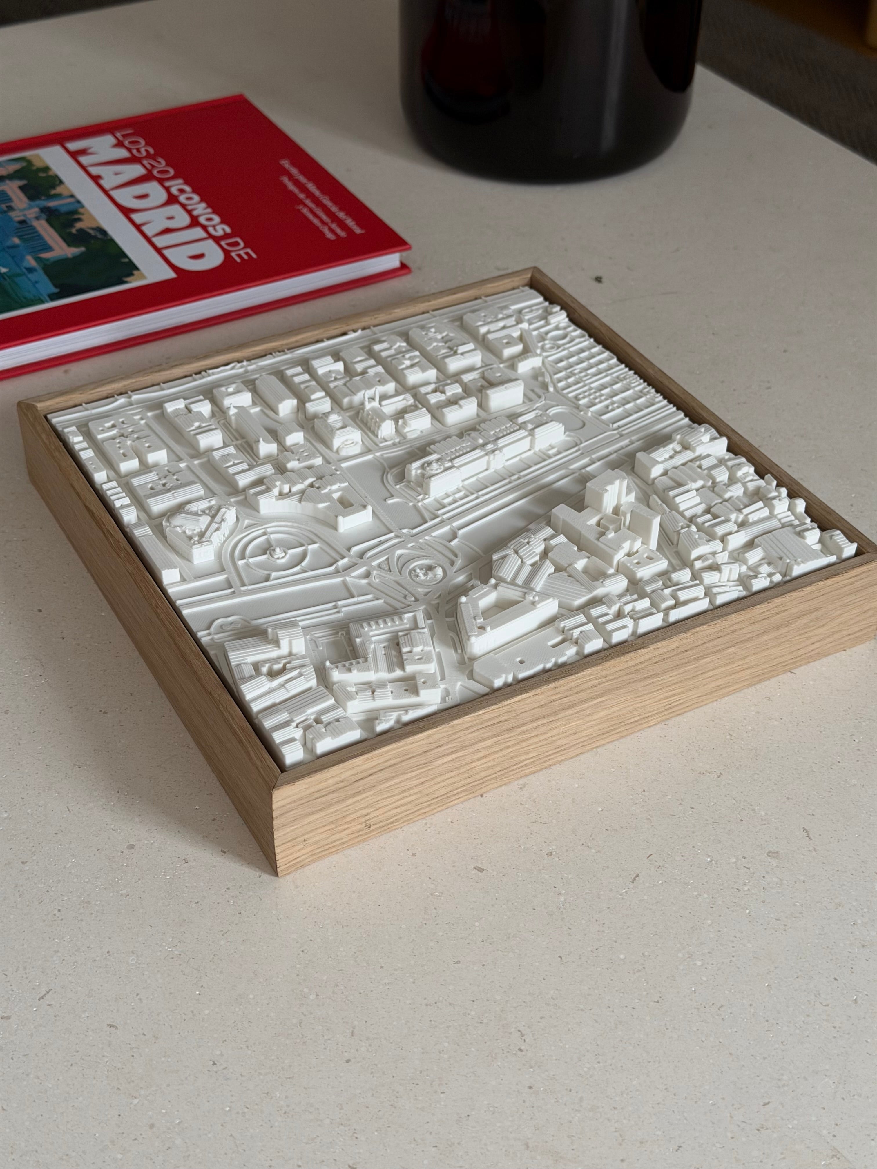 3D map of Madrid in a wooden frame on a table, next to a red Madrid guidebook