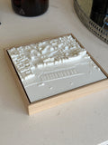 3D city map wall art in a wooden frame on a light tabletop, detailed white buildings