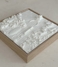 3D city map wall art in a wooden frame featuring raised white buildings and streets