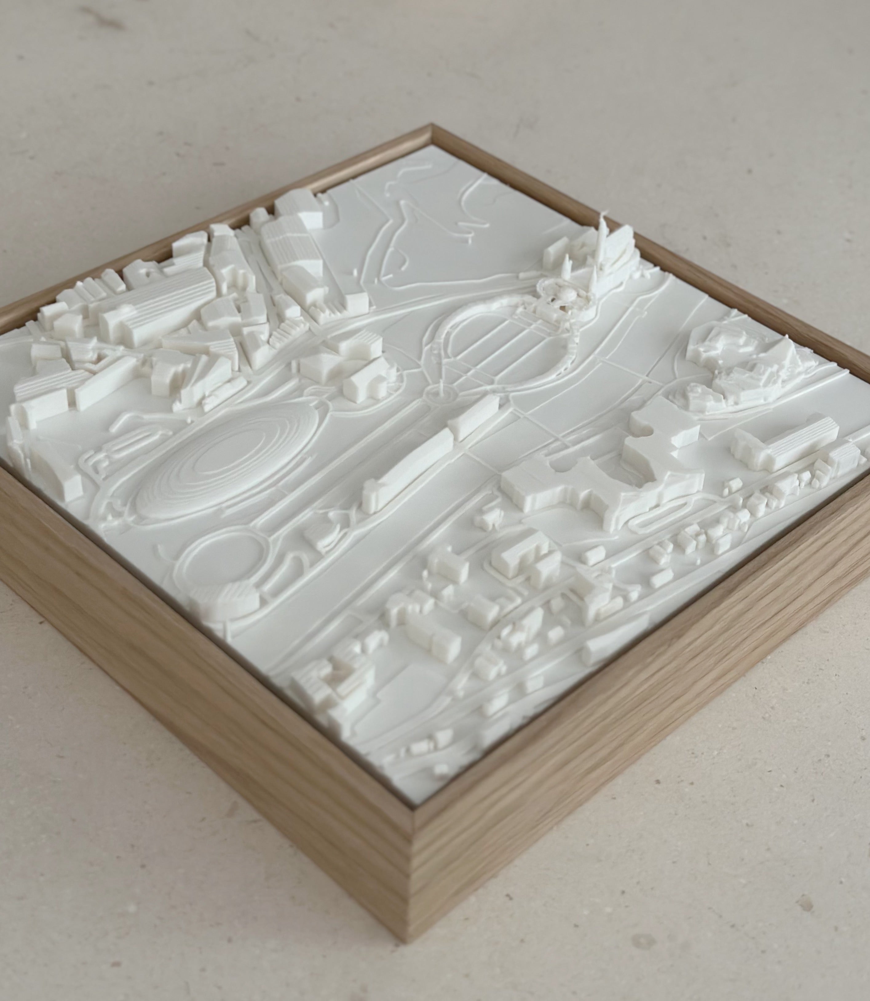 3D city map wall art in a wooden frame featuring raised white buildings and streets