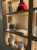Modern wooden shelf with illuminated 3D city map artwork, books, red ceramic sculpture, and decorative vases