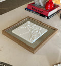Modern 3D city map art in a wooden frame on a table with decorative books