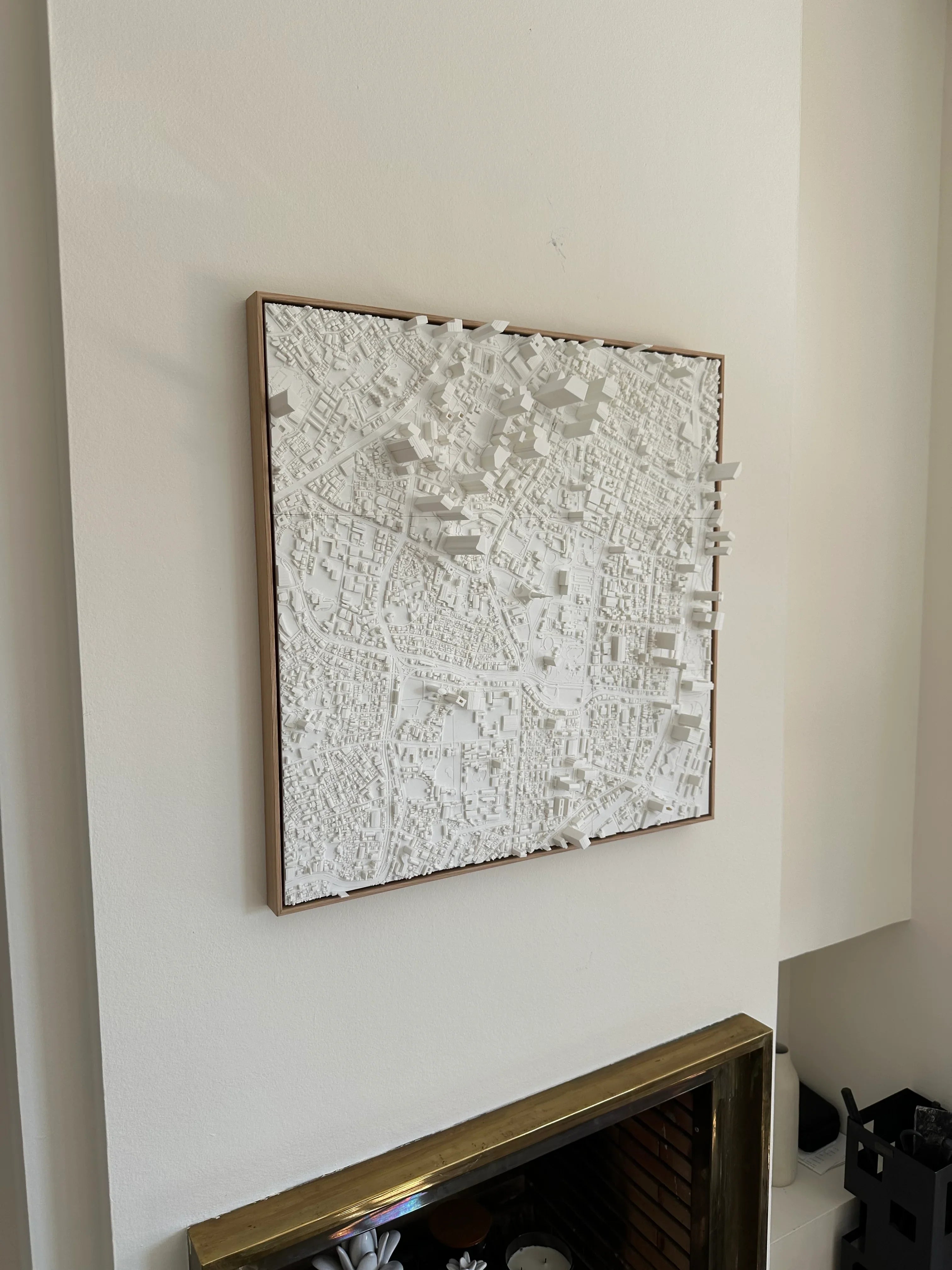 3D city map wall art in white frame above a fireplace, modern home decor