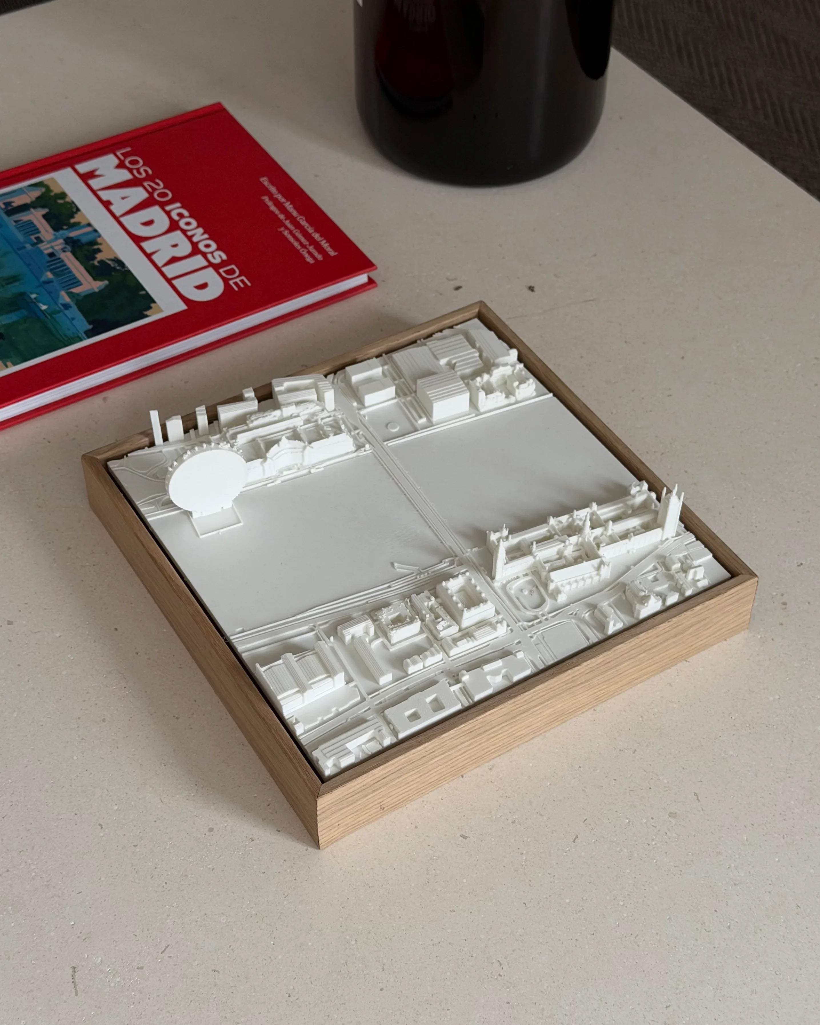 3D Madrid city map wall art in a wooden frame on a table with a red Madrid guidebook
