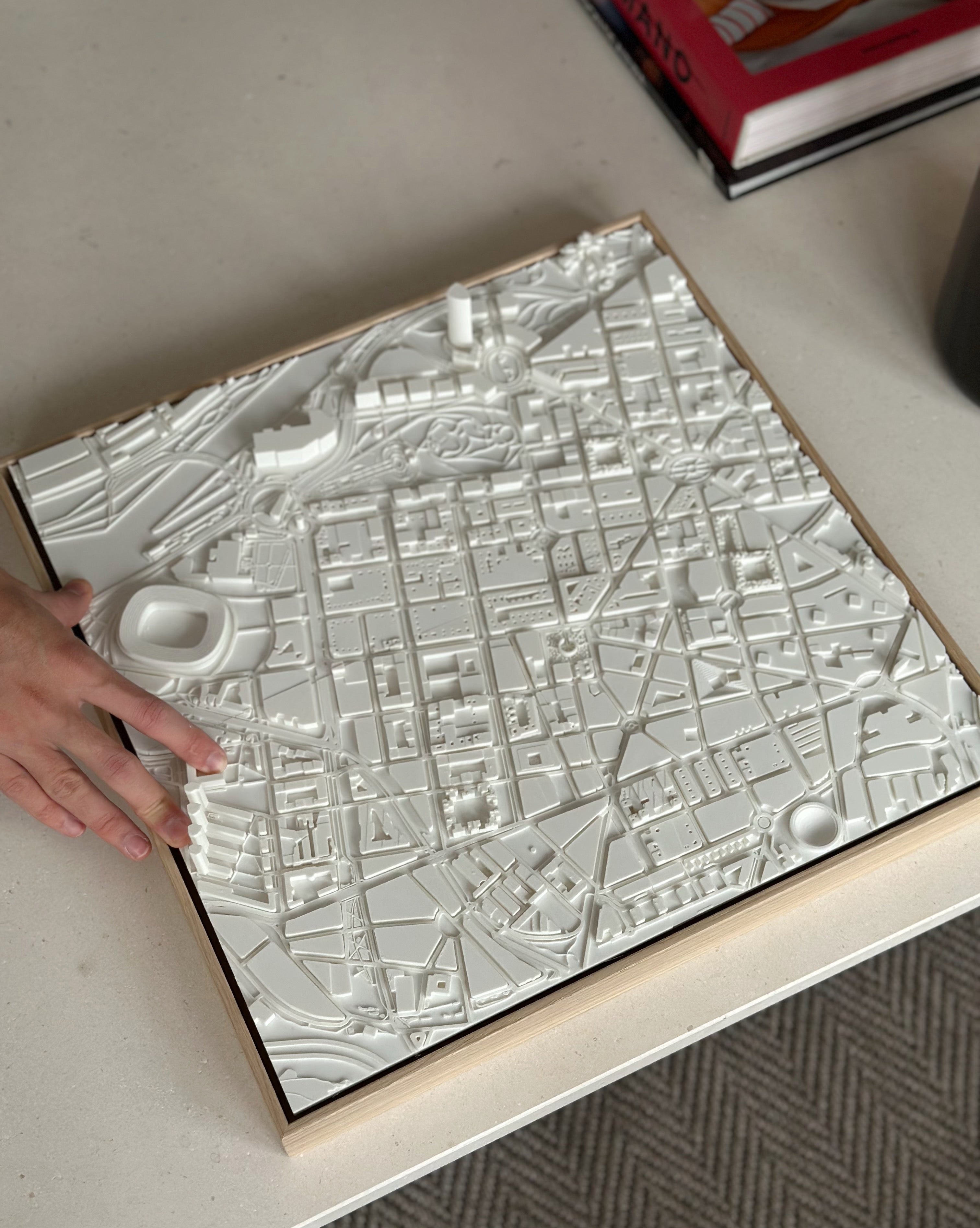 Hand touching a 3D city map wall art with white buildings and streets on a desk