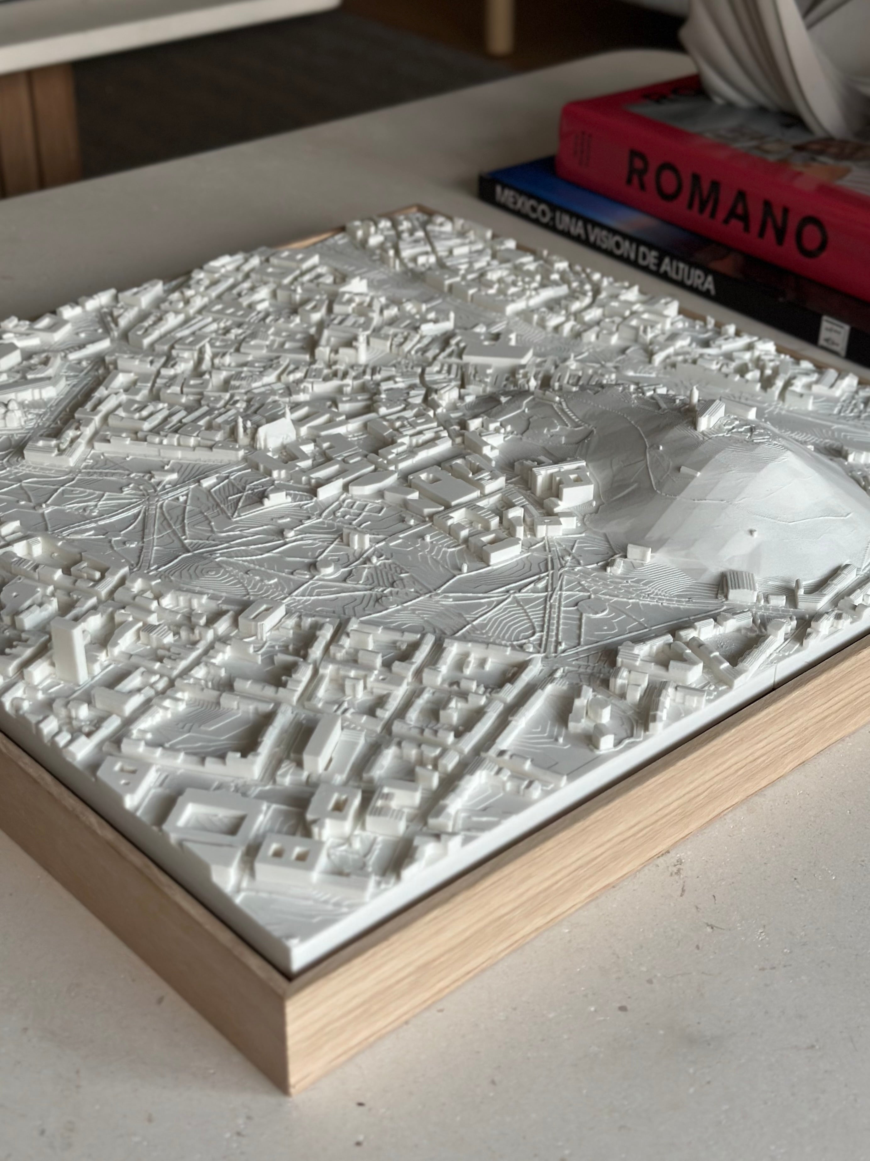 3D city map wall art in white with wooden frame, displayed on a modern table.