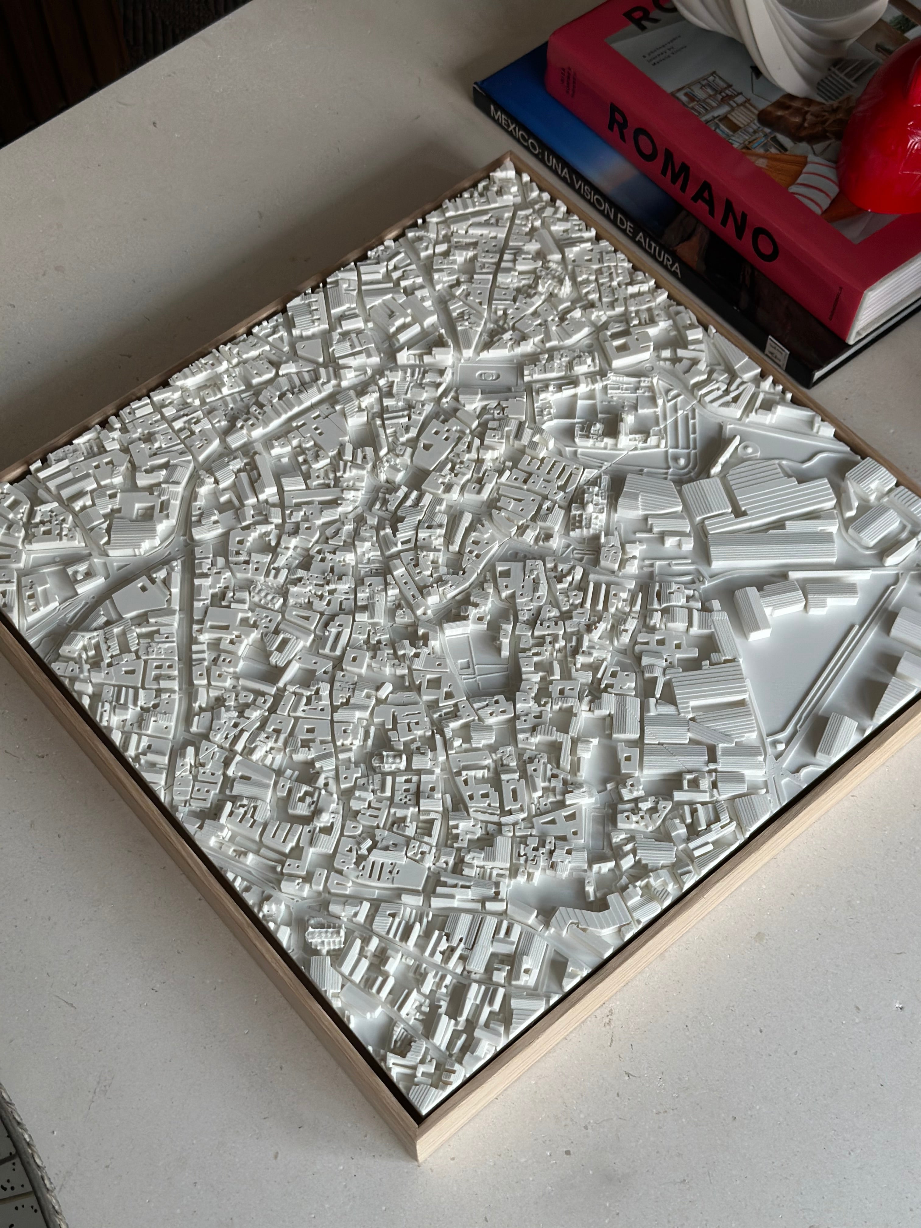 Detailed 3D city map wall art in white, displayed on a table near books.