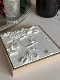 3D city map art in a wooden frame on a beige tabletop, decorative candle nearby