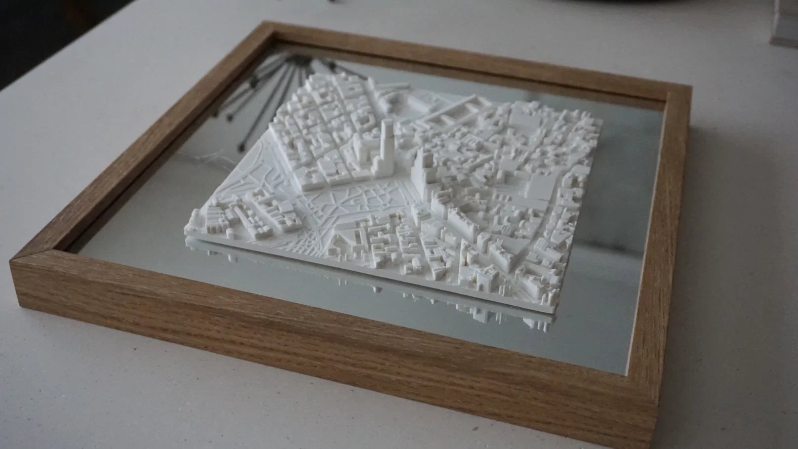 Framed 3D city map artwork with wooden border on a tabletop, urban decor piece