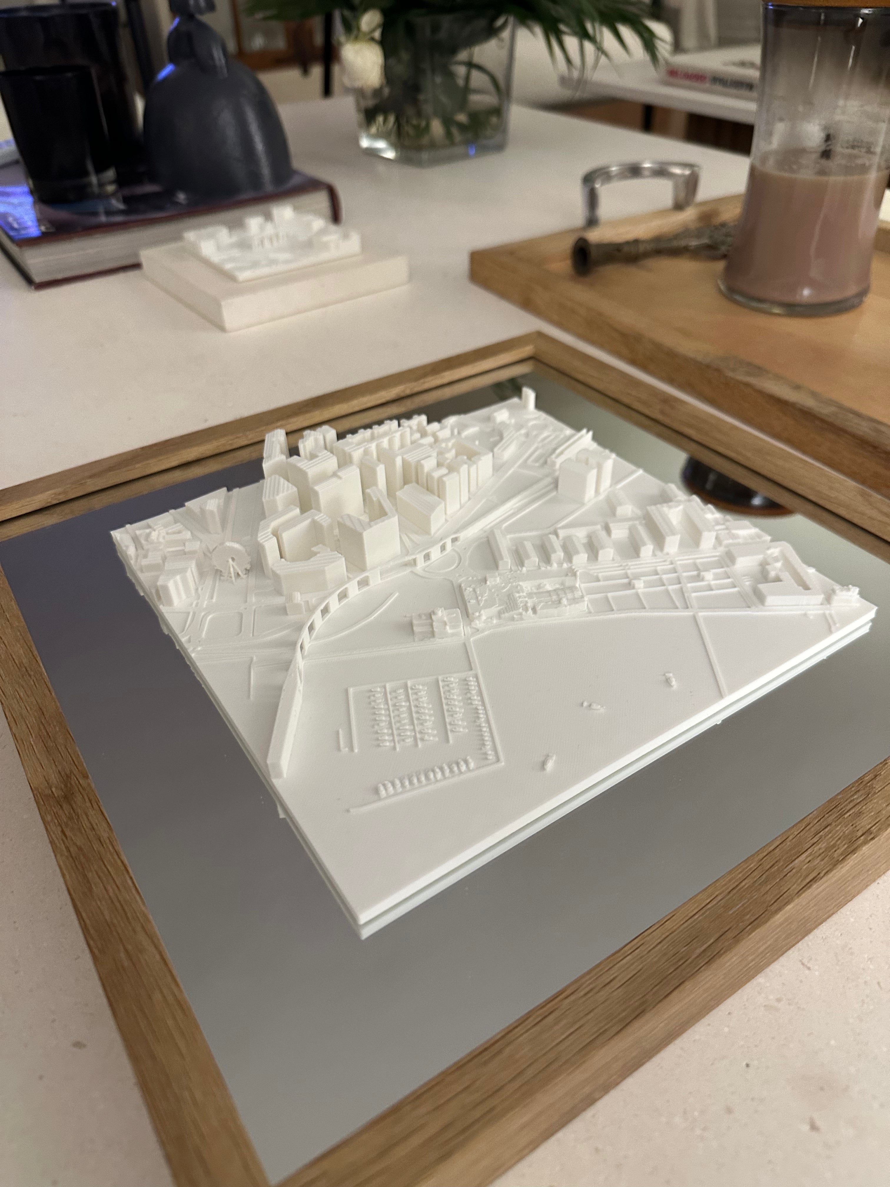 3D city map wall art in white, displayed in a wooden frame on a modern table
