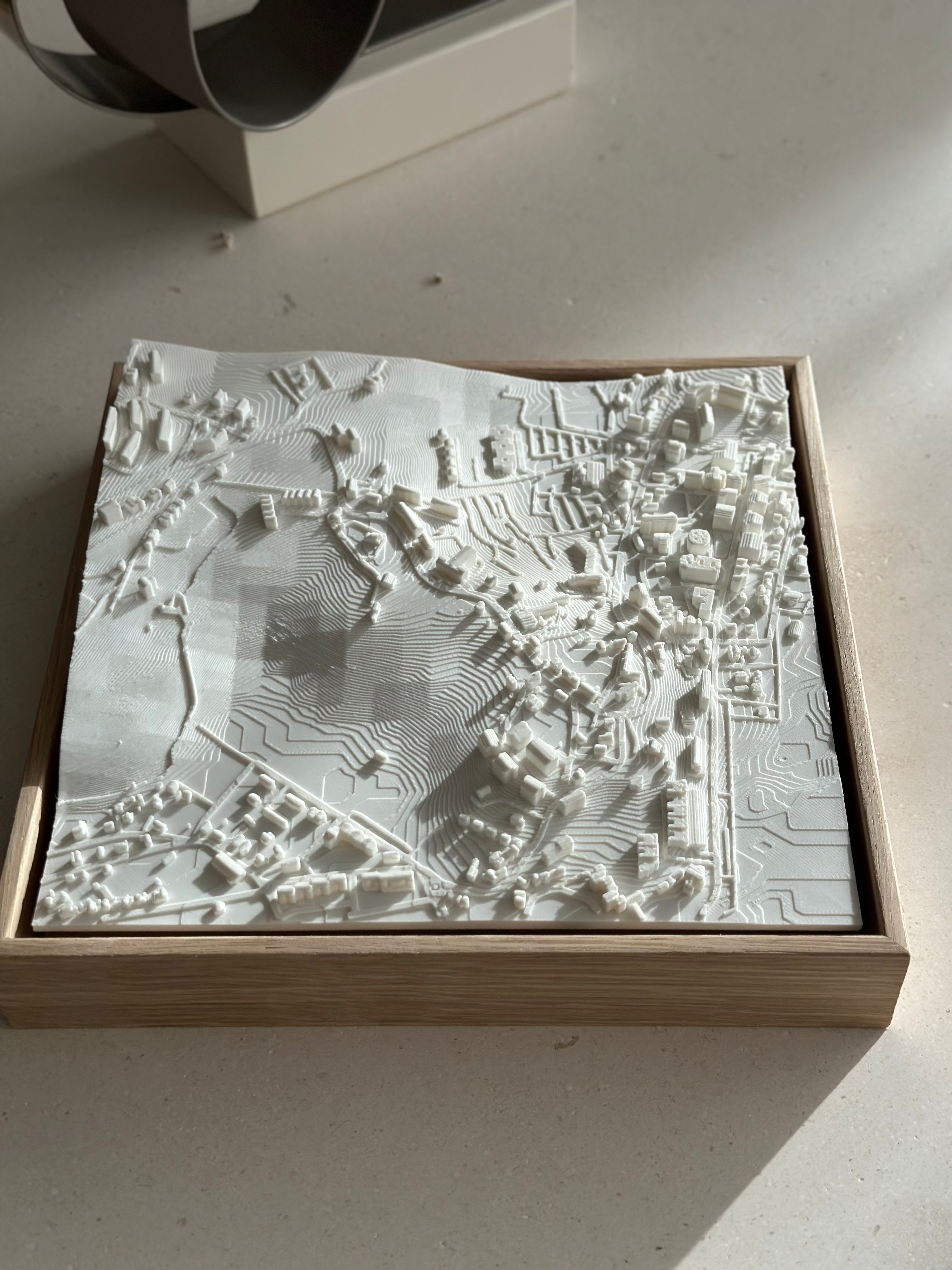 3D city map in white, framed with wood, featuring intricate topography and buildings