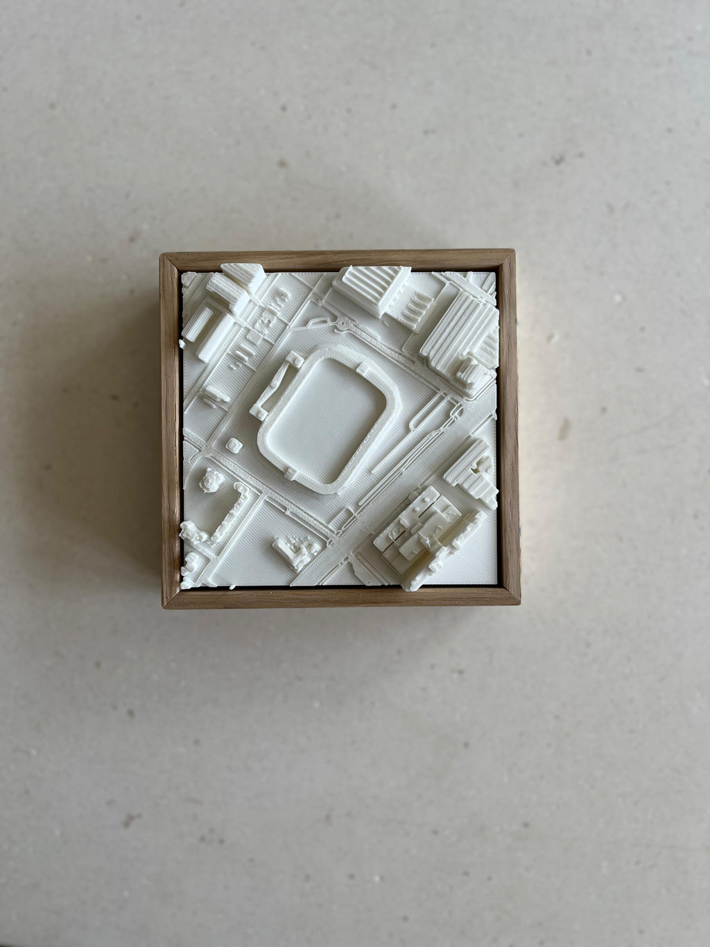 3D city map art in a wooden frame showing urban buildings and streets on a neutral background